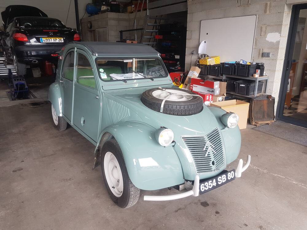 Une Citroën 2CV vert d'eau, roue de secours sur le capot, dans l'atelier
