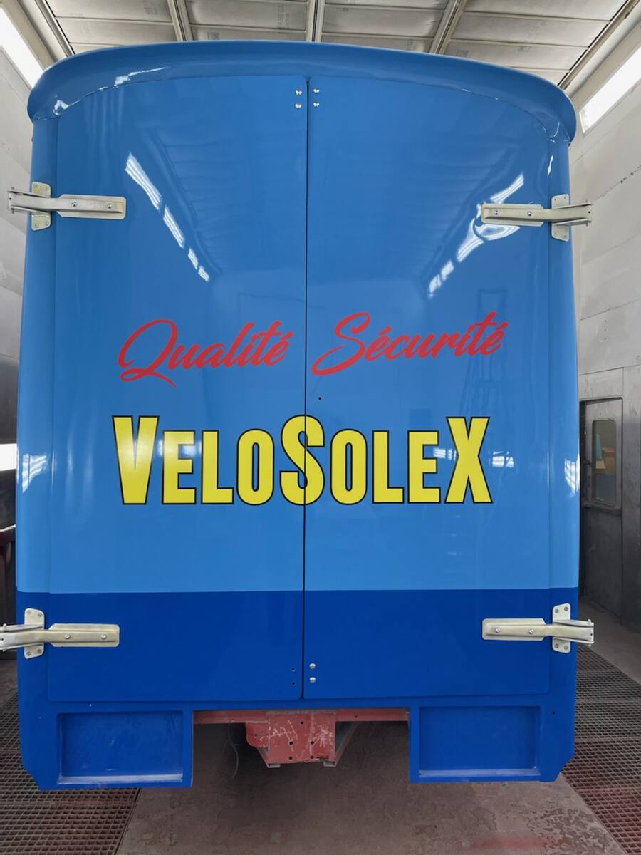 L'arrière d'un fourgon peint en bleu aux couleurs VeloSolex, dans une cabine de peinture