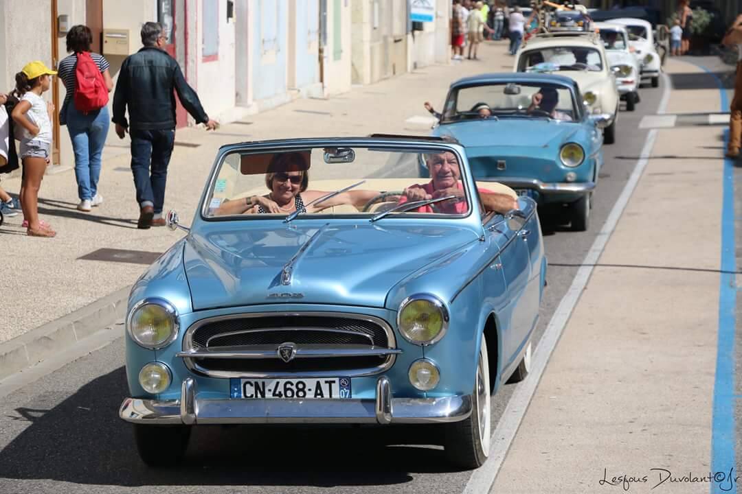Une Peugeot 403 cabriolet bleu ciel, capote baissée, dans un défilé de voitures anciennes