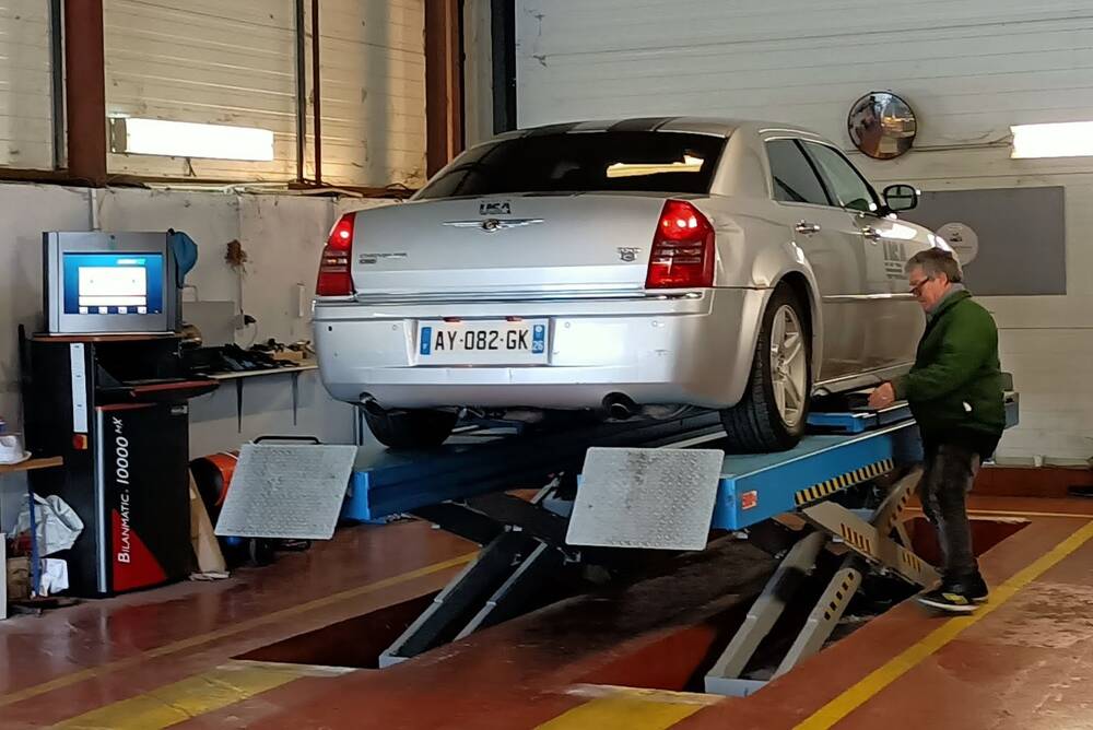 Une berline grise levée sur le pont de l'atelier, cibles de géométrie fixées sur les roues, écran de mesure à côté